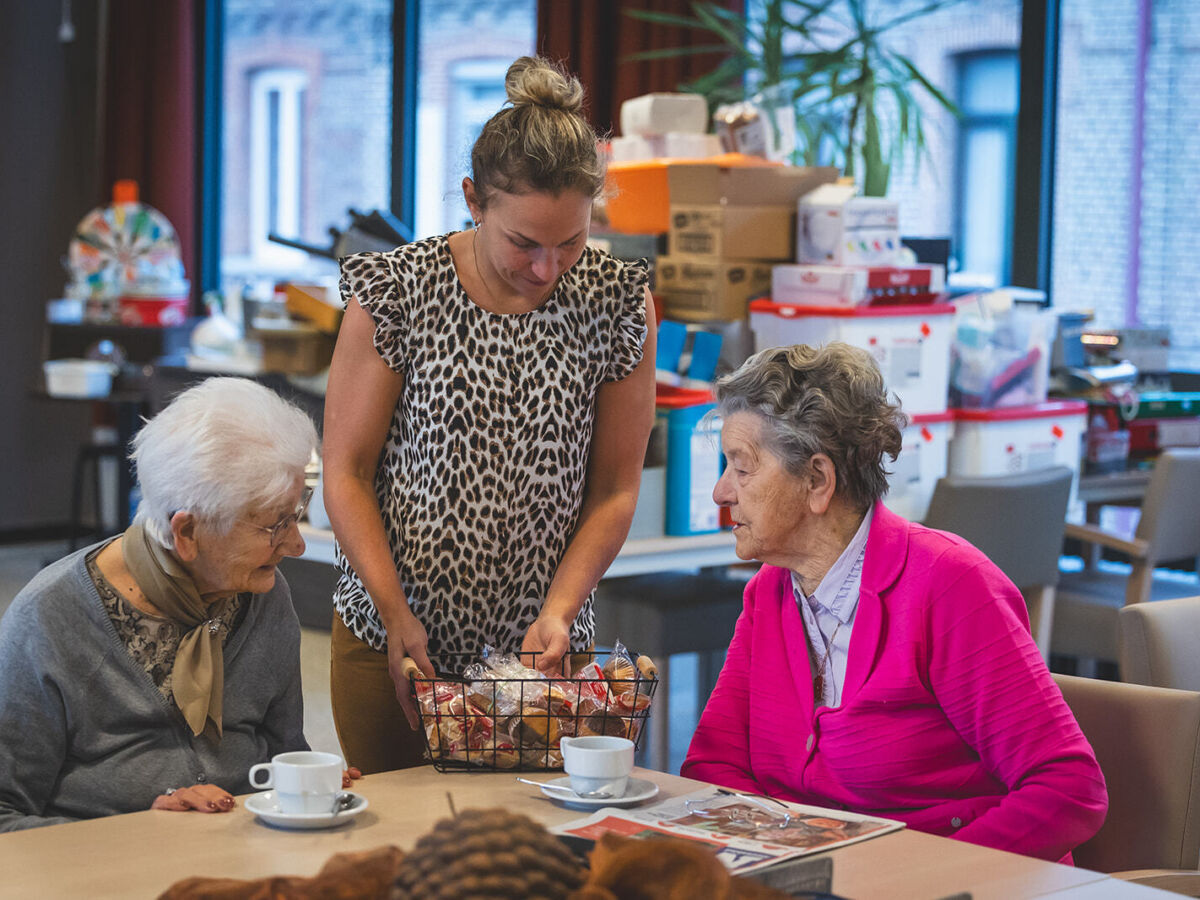 vrouwelijke medewerker biedt mand koekjes aan 2 vrouwelijke zorgvragers aan