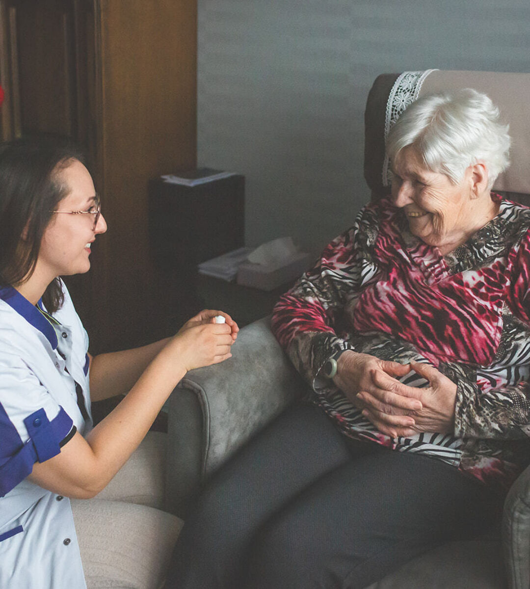 thuisverpleegster lachen naar vrouwelijke zorgvrager in zetel