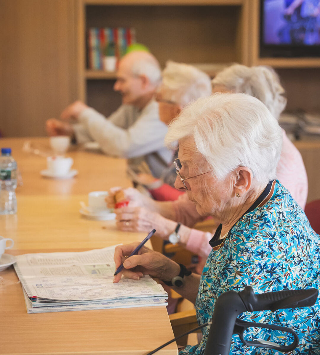 vrouwelijke zorgvrager maakt kruiswoordraadsel aan tafel in leefruimte